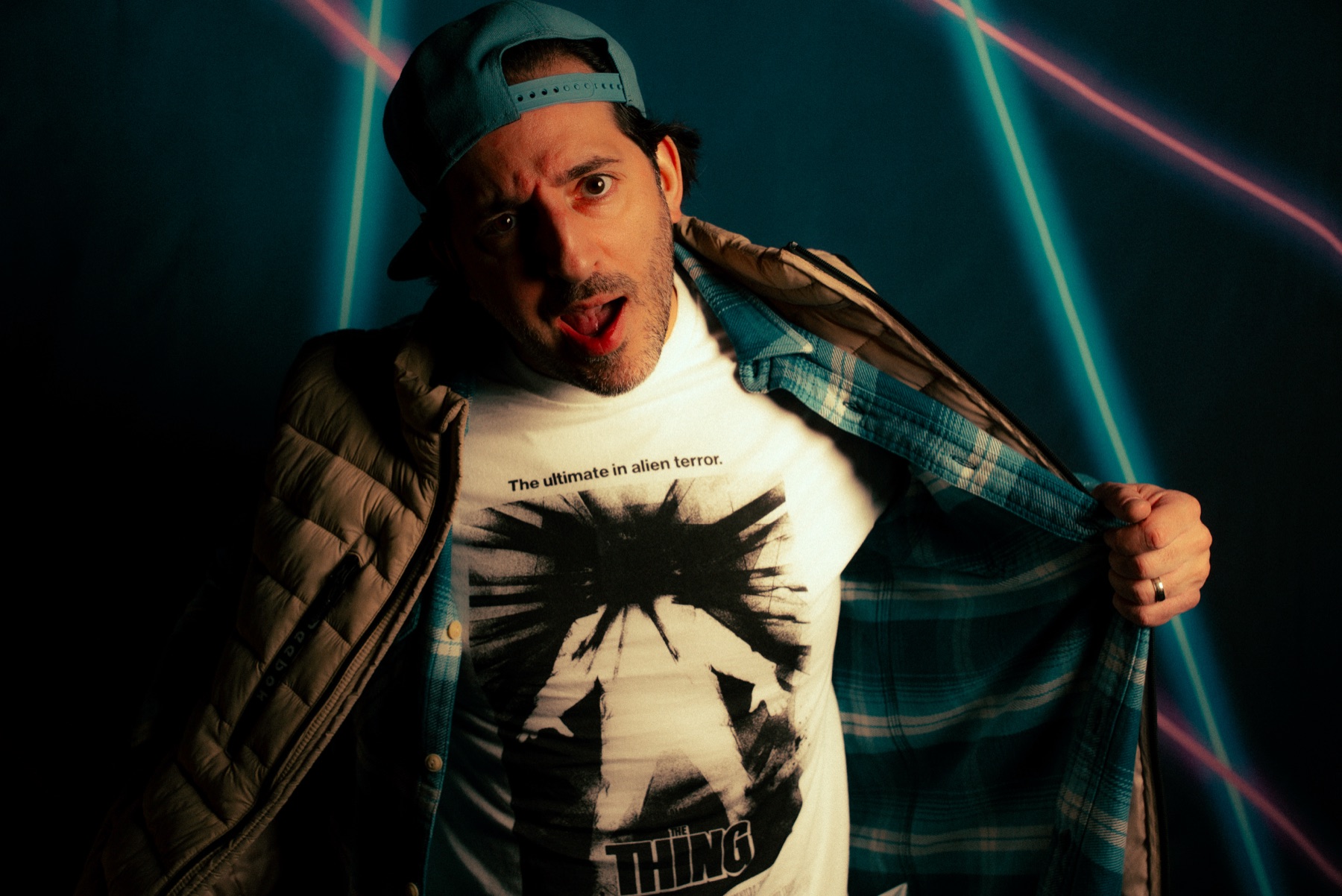 George A. Taramas opening his jacket to show a The Thing t shirt, lit by pink and blue laser lines